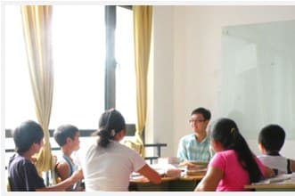 教室里几个学生围坐在长桌两侧,一名男老师在桌尾讲课